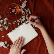 Ženske roke držijo pero in spiralno beležko kot maketo